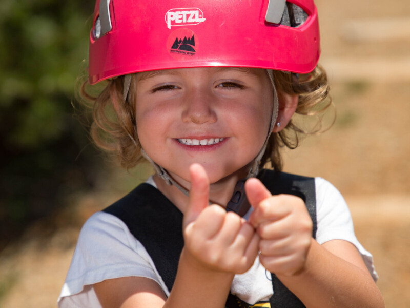 Young girl in helmet giving thumbs up sign after zipline ride